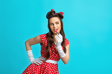 Fashionable young pinup lady in retro polka dot dress putting on makeup, applying lipstick over blue studio background