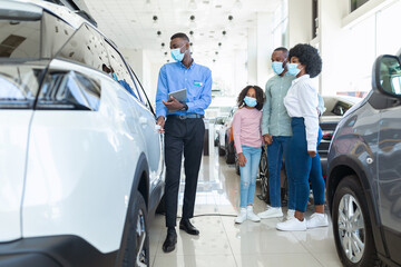 Car sales business during covid-19 quarantine. Manager talking to Afro family in masks, selling...