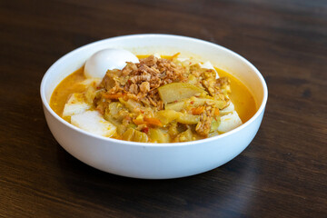 A plate of Indonesian food with vegetable curry, boiled egg and lontong rice