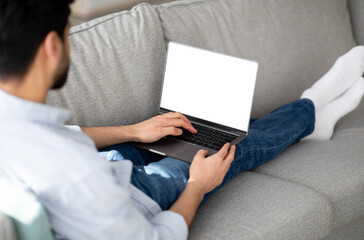 Advertisement concept. Millennial man using modern laptop with empty screen at home, mockup for your website or design