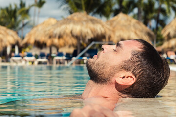 Man with stubble on the face relaxes in the water pool enjoying the sun. Serene man concept.