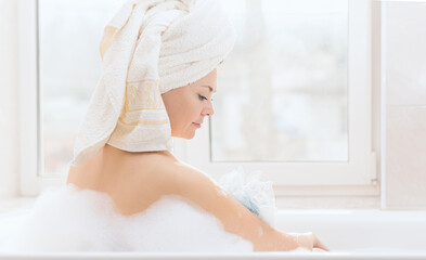 Young woman takes a bath with lush foam near the window. Personal hygiene, healthcare concept