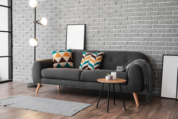 Stylish dark sofa with blank poster near brick wall