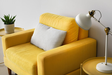 Yellow armchair, coffee tables with lamp and houseplant near light wall