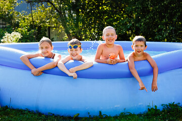 Summer season concept background. Four happy friends in an inflatable pool in the garden, refreshing themselves in hot weather.