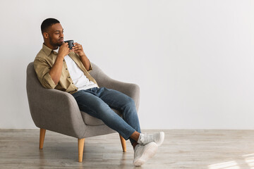 Black Man Enjoying Coffee Sitting In Chair On Gray Background