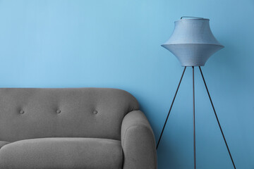 Stylish standard lamp and sofa near blue wall