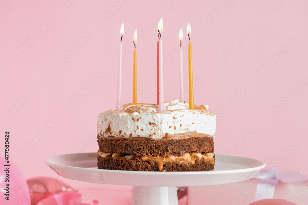 Wall mural Stand with tasty birthday cake and burning candles on pink background