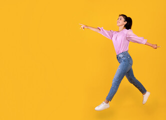 Fototapeta na wymiar Excited armenian woman running and showing copy space over yellow studio background, empty space
