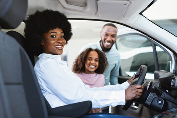 Test drive. Black woman sitting in driver seat of new car, choosing vehicle with husband and...