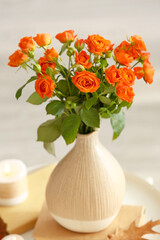 Vase with beautiful orange roses, books and candles on table in room