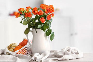 Jug with beautiful orange roses and pumpkins in room