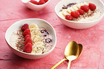 trendy breakfast bowl with oatmeal porridge, fresh raspberries, banana, chia seeds, linseed and jam on magenta surface