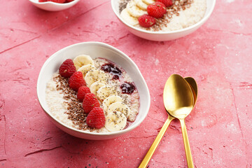 trendy breakfast bowl with oatmeal porridge, fresh raspberries, banana, chia seeds, linseed and jam on magenta surface