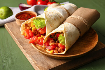 Board of tasty Mexican burritos with vegetables on green wooden background