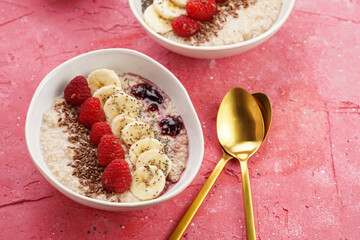 trendy breakfast bowl with oatmeal porridge, fresh raspberries, banana, chia seeds, linseed and jam on magenta surface