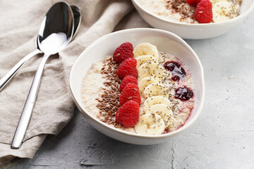 Trendy breakfast bowl with oatmeal porridge, fresh raspberries, banana, chia seeds, linseed and jam