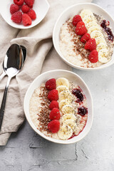 Trendy breakfast bowl with oatmeal porridge, fresh raspberries, banana, chia seeds, linseed and jam