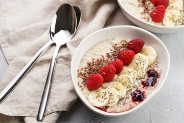 Trendy breakfast bowl with oatmeal porridge, fresh raspberries, banana, chia seeds, linseed and jam