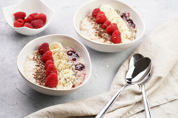 Trendy breakfast bowl with oatmeal porridge, fresh raspberries, banana, chia seeds, linseed and jam