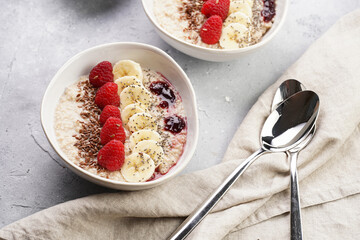 Trendy breakfast bowl with oatmeal porridge, fresh raspberries, banana, chia seeds, linseed and jam