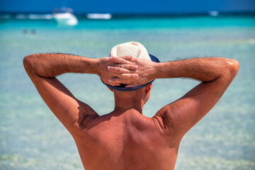 Back view of a man wearing straw hat on the shoreline. Holiday concept.