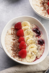 Trendy breakfast bowl with oatmeal porridge, fresh raspberries, banana, chia seeds, linseed and jam