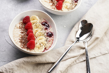 Trendy breakfast bowl with oatmeal porridge, fresh raspberries, banana, chia seeds, linseed and jam