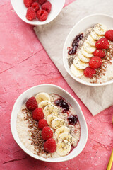 trendy breakfast bowl with oatmeal porridge, fresh raspberries, banana, chia seeds, linseed and jam on magenta surface