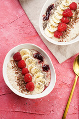 trendy breakfast bowl with oatmeal porridge, fresh raspberries, banana, chia seeds, linseed and jam on magenta surface