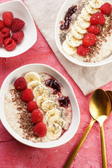 trendy breakfast bowl with oatmeal porridge, fresh raspberries, banana, chia seeds, linseed and jam on magenta surface