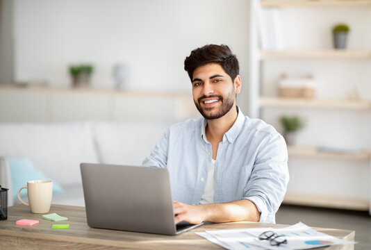 Millennial Freelancer. Portrait Of Happy Arab Man Sitting At Desk With Laptop, Working At Home Office, Copy Space