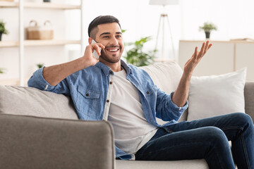Portrait of smiling millennial man talking on phone at home