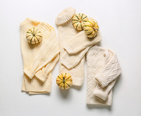 Warm children's sweaters and pumpkins on white background