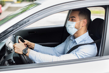 Middle-eastern businessman in face mask driving car, side view