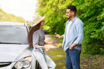 Positive arab man and woman standing by automobile, having conversation