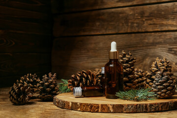 Board with bottles of essential oil and pine cones on wooden background