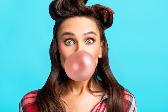 Emotional young pin up woman in retro clothes blowing bubble from chewing gum over blue studio background