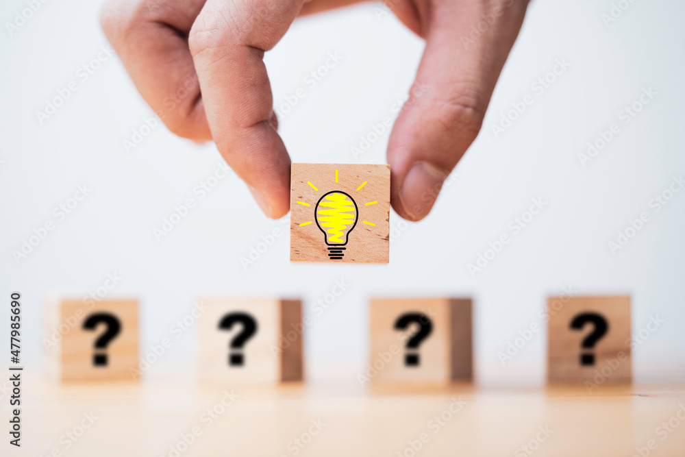 Poster hand putting lightbulb on wooden cube block in front of question mark for question and answer concep
