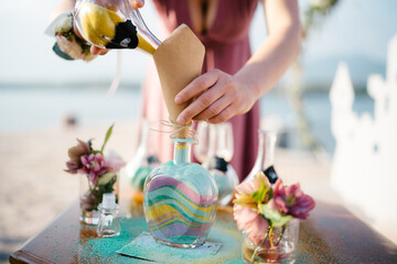 Bride pours yellow sand in layers into a glass jar