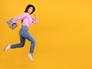 Excited young armenian woman running with laptop computer in hand, having fun on yellow studio background, copy space