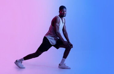 Full length of sporty black man doing lunges or stretching his legs in neon light. Active lifestyle concept