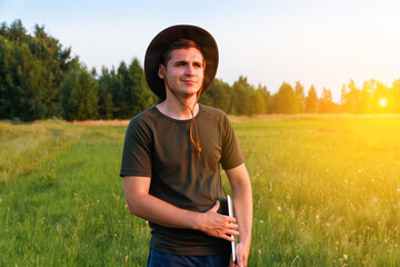 Young man smile farmer in cowboy hat at agricultural field on sunset holding tablet. Male on grass background, outdoors in meadow. Agriculture concept. Digital farmland. Smart agronomist. Copy space