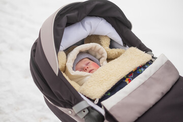 Caucasian baby sleeping in stroller at winter snowy day.
