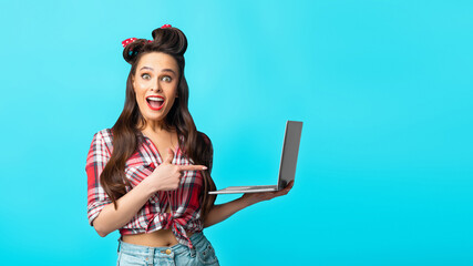 Excited pinup woman in retro style wear pointing at laptop computer over blue background, banner design with free space