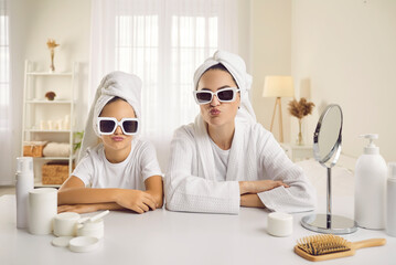 Portrait of beautiful mother and daughter wearing cool trendy shades and white bath towels duck...