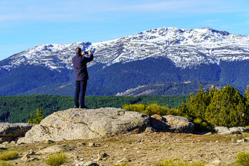 Man climbed on a rock and taking photos with his mobile to the mountains. Morcuera Madrid.