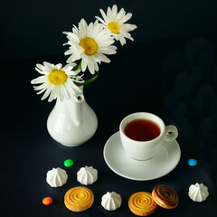 Tea cup , sweets and a bouquet of white daisies on a black background.