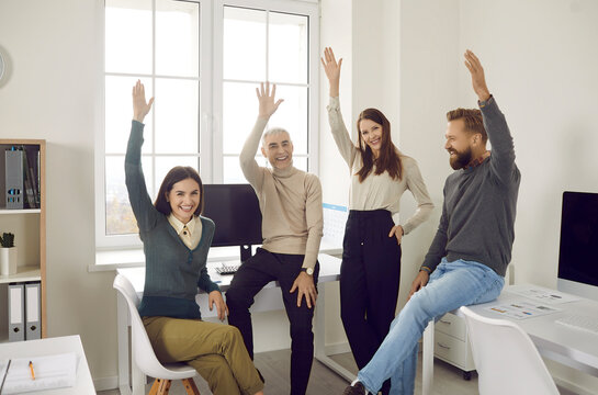 Team of happy, confident, motivated, enthusiastic male and female company employees smiling and raising their hands to vote for a good business suggestion during a casual corporate meeting