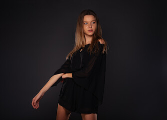 Pretty brunette girl with little black dress posing isolated on dark background in studio
